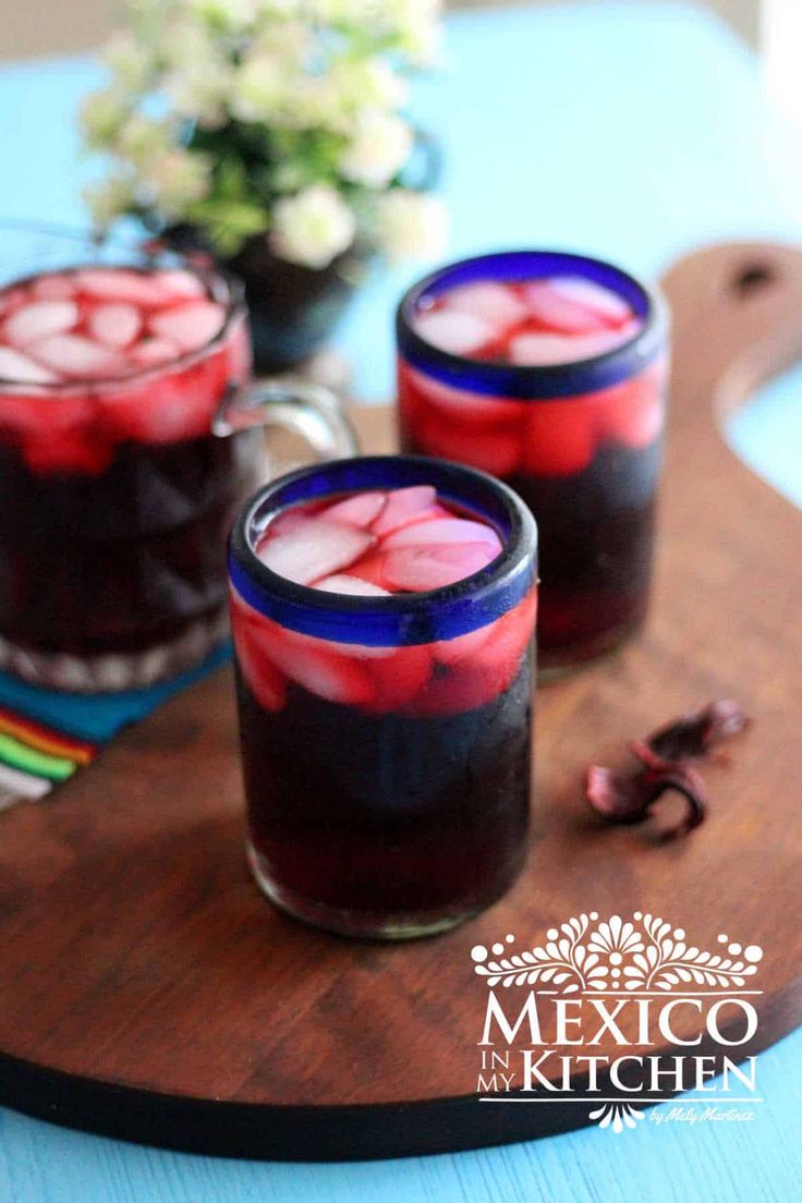 two glasses filled with liquid sitting on top of a wooden cutting board next to a potted plant