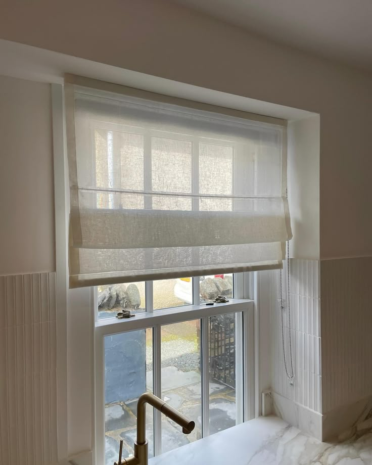 a bathroom window with roman shades and a sink in front of the window is shown