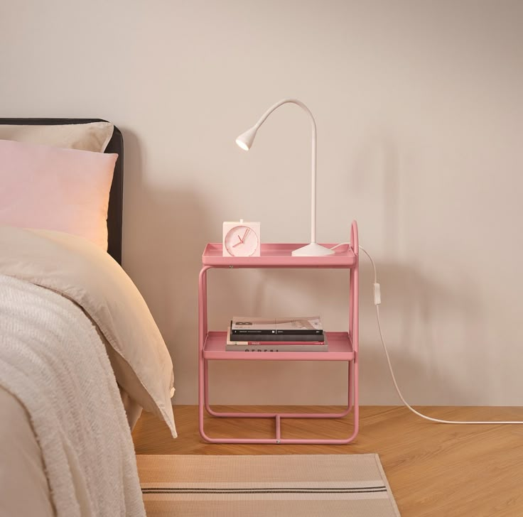 a pink shelf next to a bed with a white lamp on it and a rug