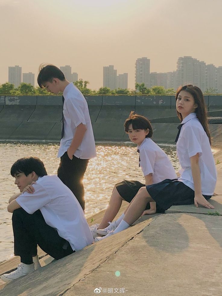 four people sitting on the edge of a body of water