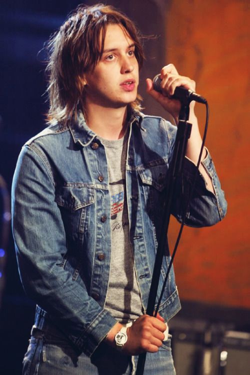 a young man in denim jacket holding a microphone and looking at the camera while standing on stage