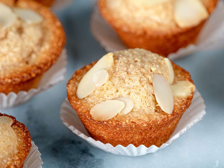 several muffins with almonds in them sitting on a blue tablecloth covered surface