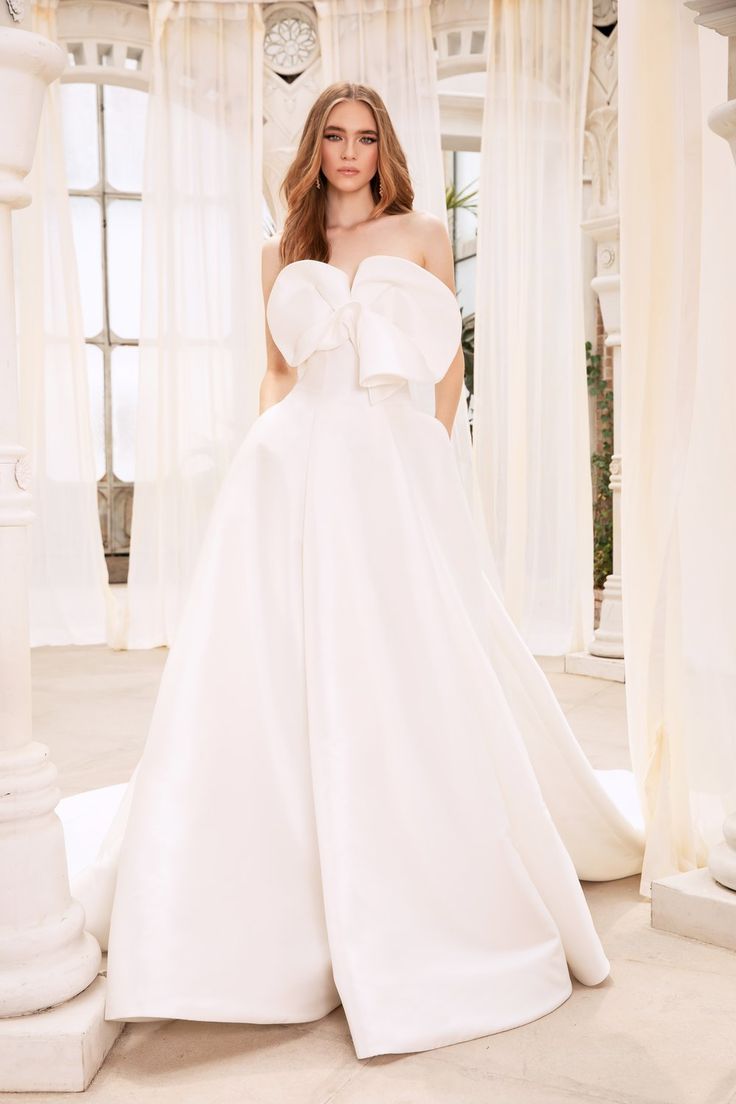 a woman in a white wedding dress standing on the floor with her hands behind her back