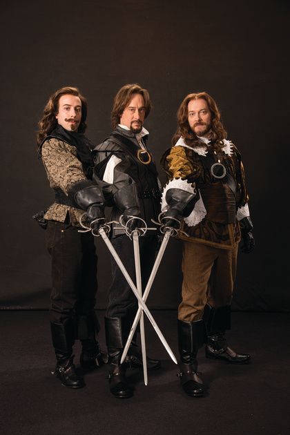 three men dressed in medieval costumes posing for a photo with swords and armor on their shoulders