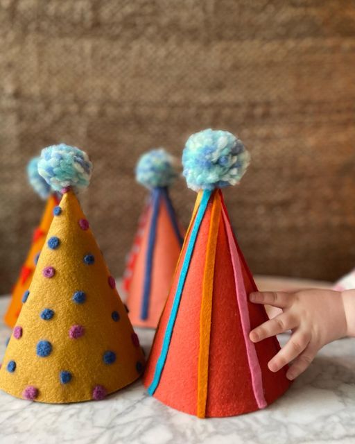 a child's hand is reaching for three colorful party hats with pom poms