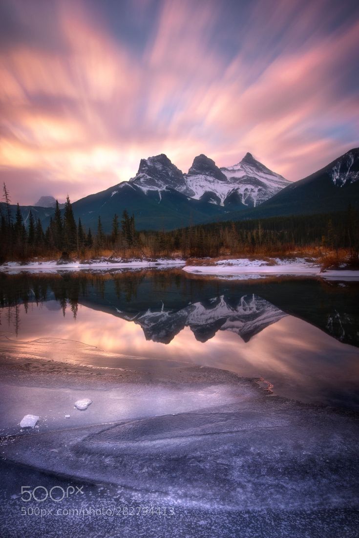 the mountains are reflected in the still water at sunset, with snow on the ground