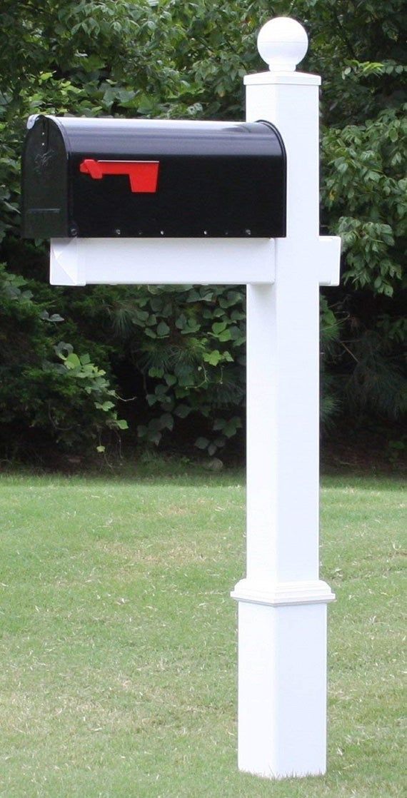 a white mailbox with a red letter on it in the grass near some trees