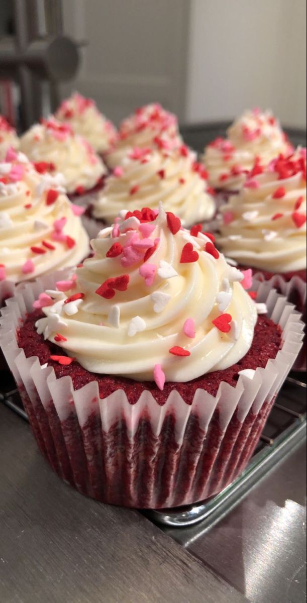 red velvet cupcakes with white frosting and sprinkles on a cooling rack