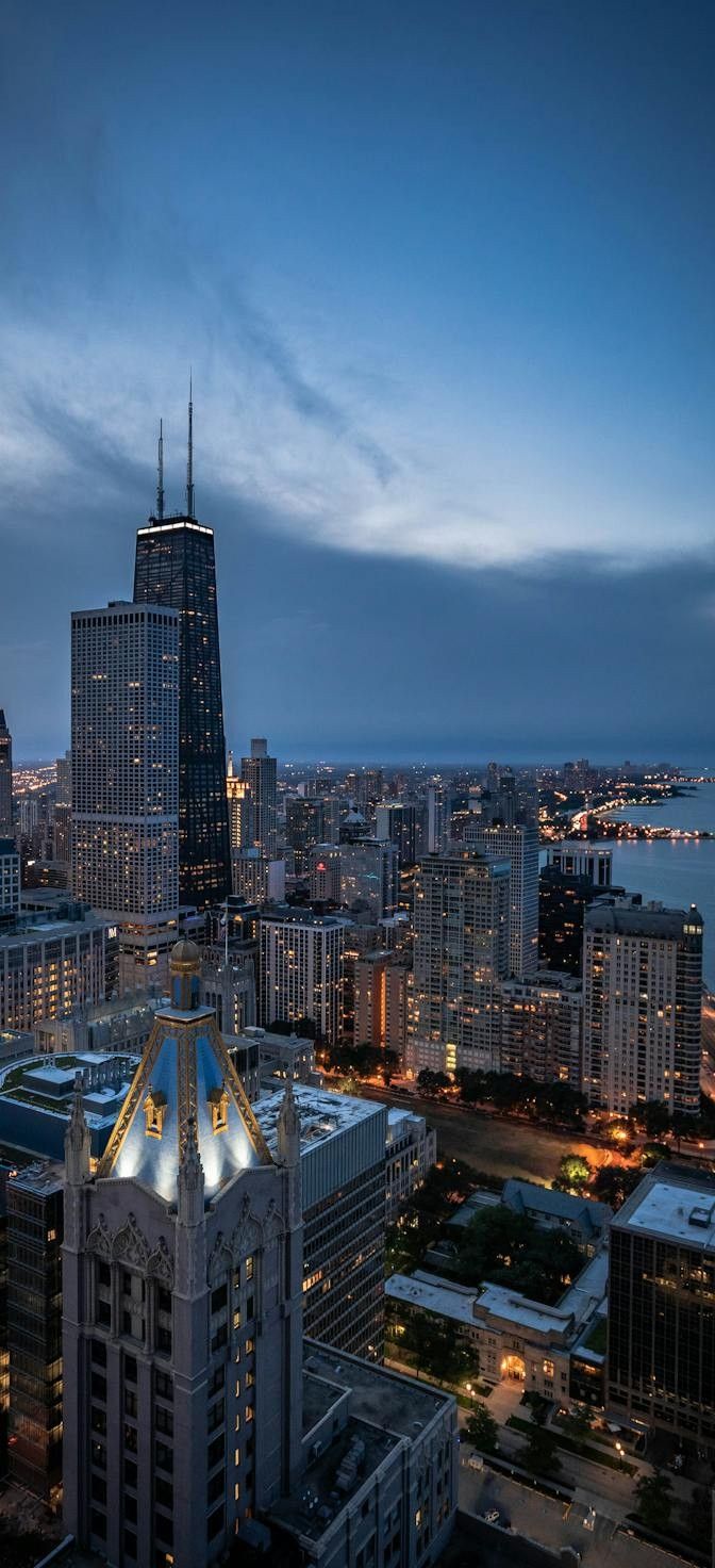 the city skyline is lit up at night with skyscrapers in the foreground and water below