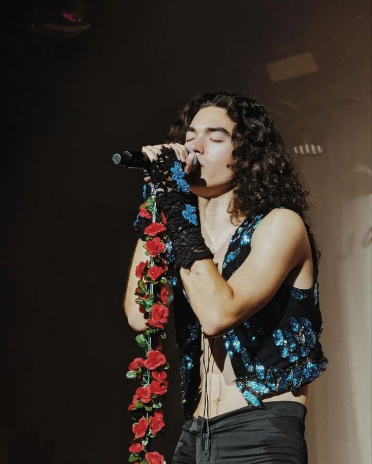 a man with long curly hair holding a microphone in his right hand and singing into the microphone