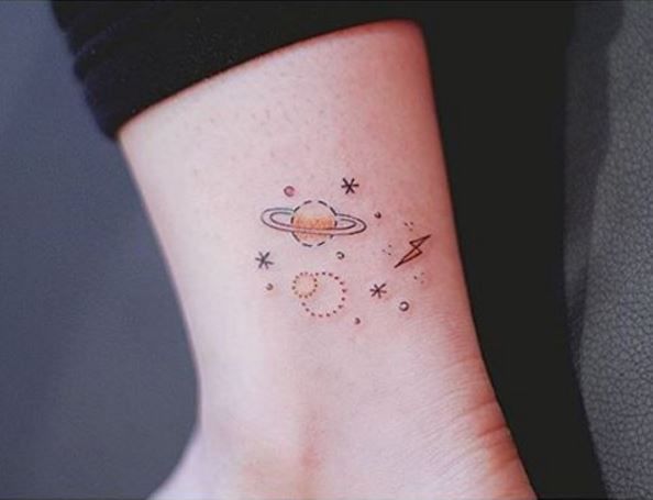 small saturn tattoo on the wrist with stars and planets in space around it, as seen from above