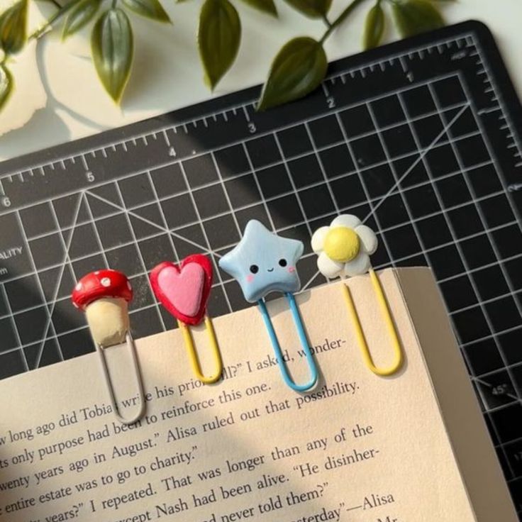 three little bookmarks are placed on top of an open book with paper clips attached to them