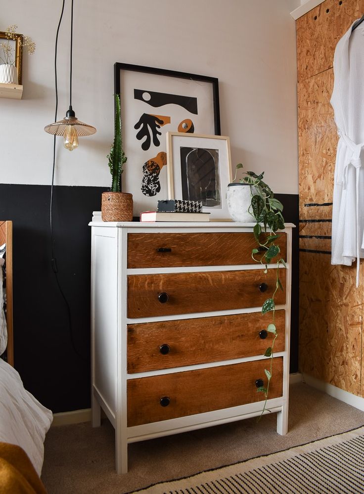 a white dresser sitting next to a bed with pictures on top of it and plants growing out of the drawers