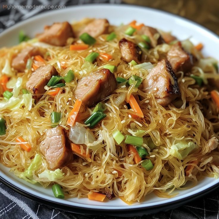 a white plate topped with noodles and meat on top of a bed of veggies