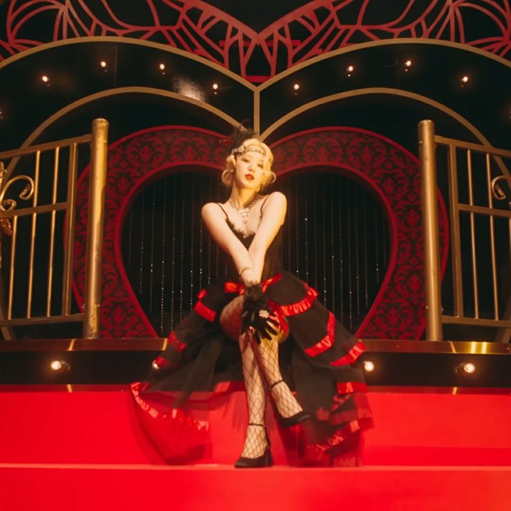 a woman sitting on top of a red stage wearing black and white clothes with her legs crossed