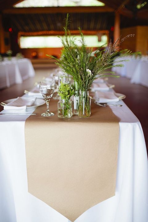 the table is set with white linens and greenery in vases on top