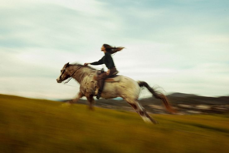 a woman riding on the back of a white horse through a green grass covered field