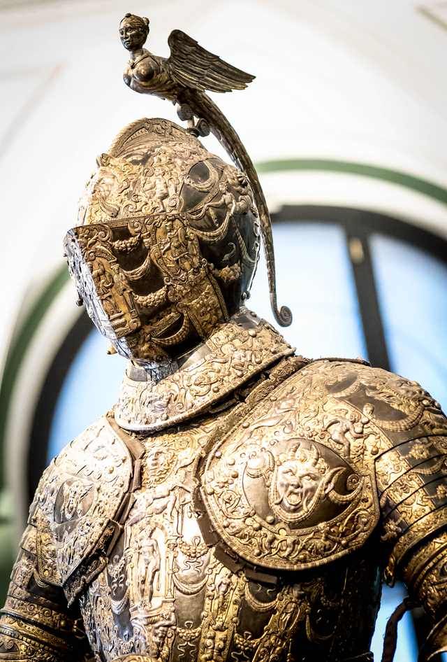 a close up of a gold armor on display in front of a circular glass window