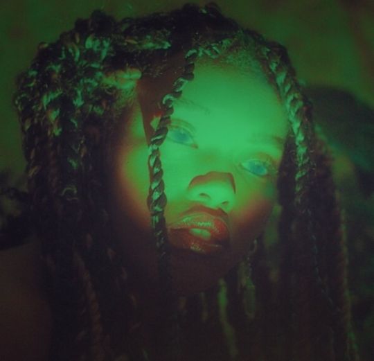 a woman with green light on her face and braids in front of the camera