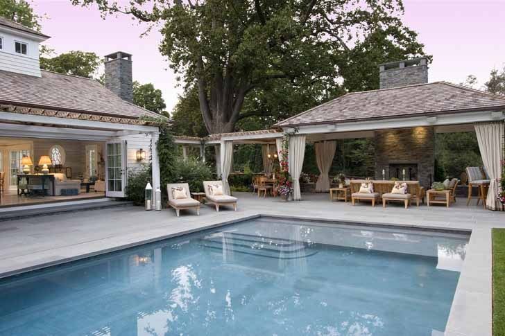 an outdoor pool with patio furniture and covered in curtains next to a house at dusk