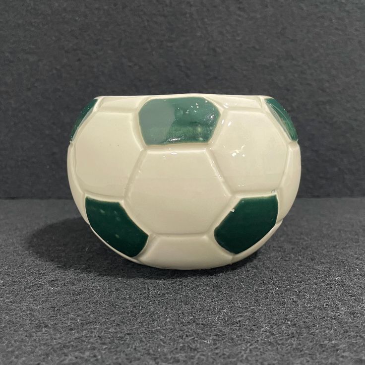 a white and green soccer ball sitting on top of a gray table next to a black wall