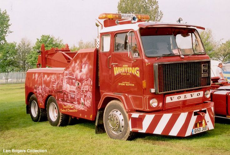 a large red truck parked on top of a lush green field next to other trucks