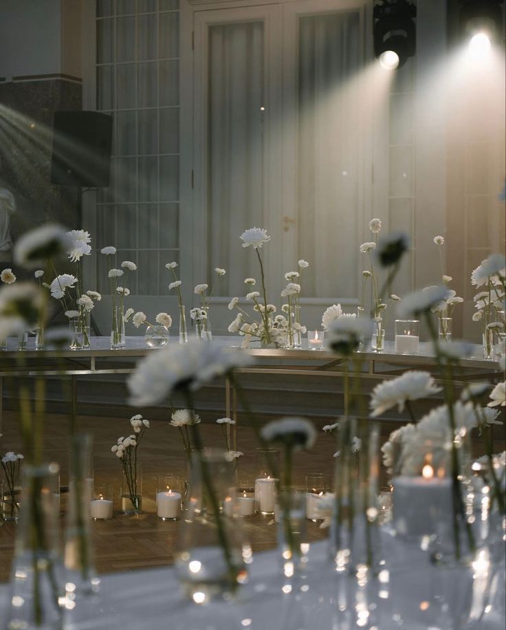 white flowers in vases sitting on top of a table next to candles and windows