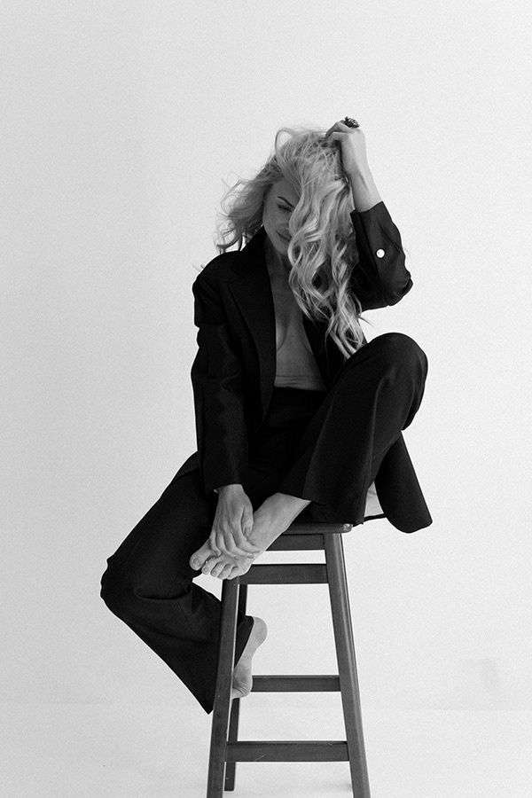 a black and white photo of a woman sitting on a stool with her legs crossed