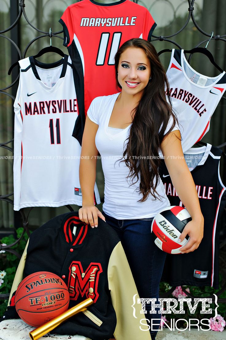 a young woman holding a volleyball and ball in front of some sports jersey hanging on a fence