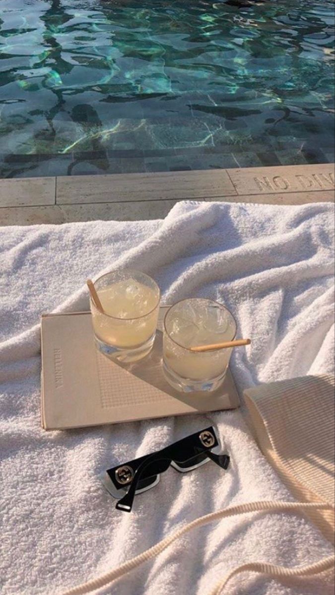 two glasses on a towel next to a swimming pool