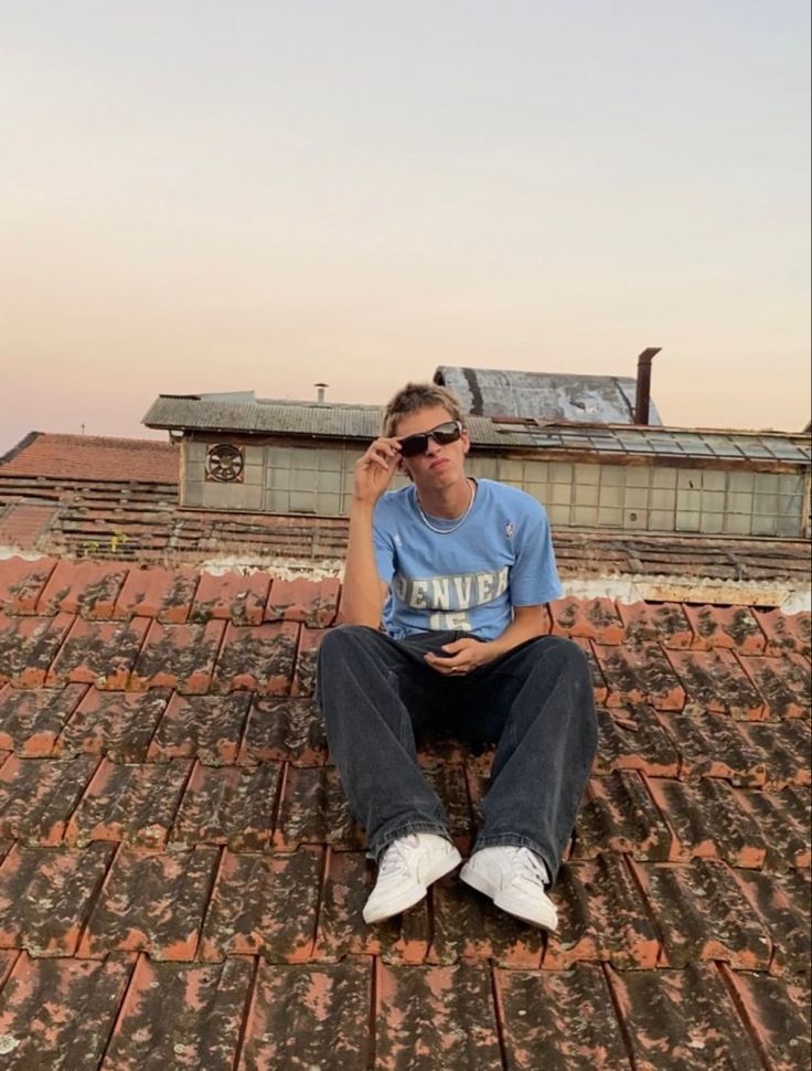 a man sitting on top of a roof talking on a cell phone while wearing sunglasses