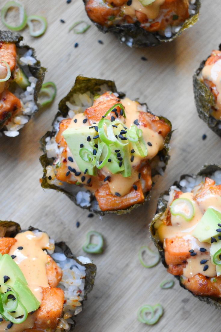 several sushi shells with salmon and avocado in sauce on the top one is topped with black sesame seeds