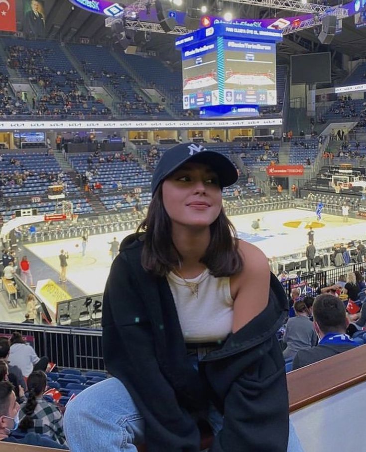 a woman sitting in the bleachers at a basketball game wearing a black hat