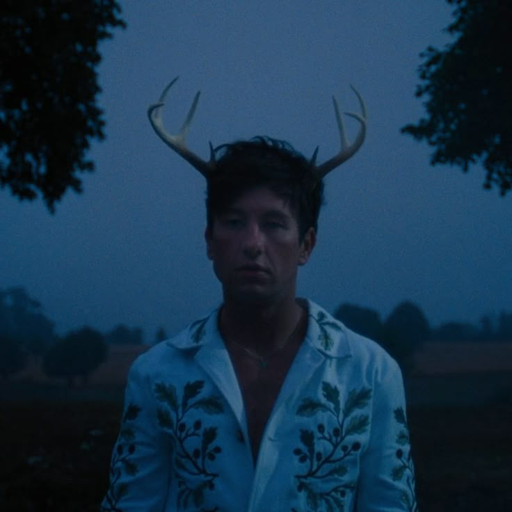 a man with antlers on his head standing in front of some trees at night