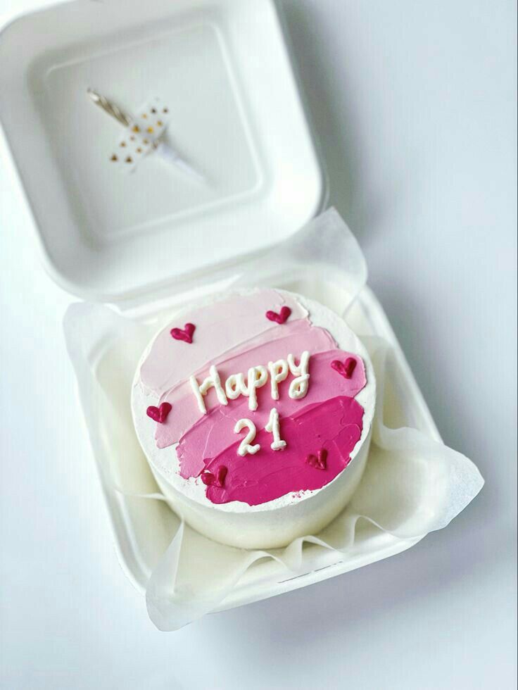 a birthday cake with pink frosting and hearts on it in a plastic container, ready to be eaten