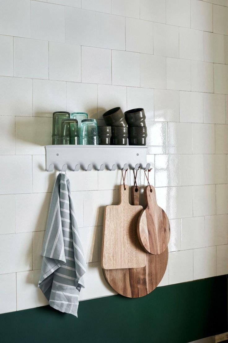 two wooden cutting boards hanging on a white brick wall next to green and white tiles