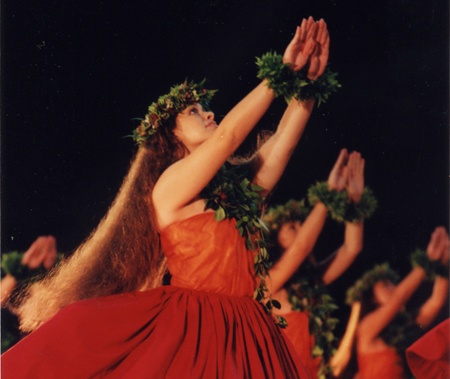 a woman in a red dress is holding her hands up to the sky with other dancers behind her