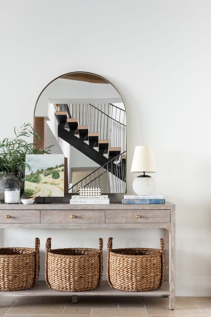 a console table with baskets under it and a mirror above it, next to a staircase