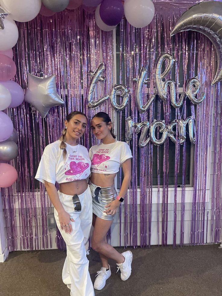 two women standing next to each other in front of balloons