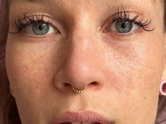 a close up of a woman with freckles and piercings on her nose