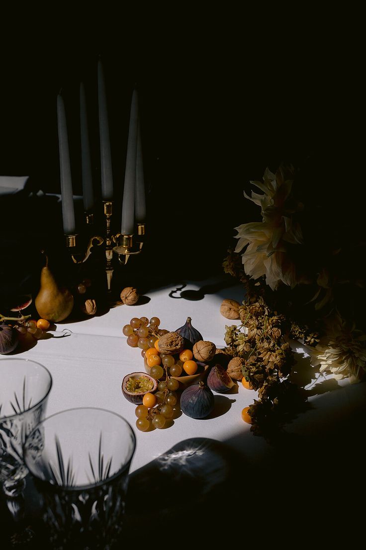 a table topped with lots of fruit and glasses next to candles on top of a table