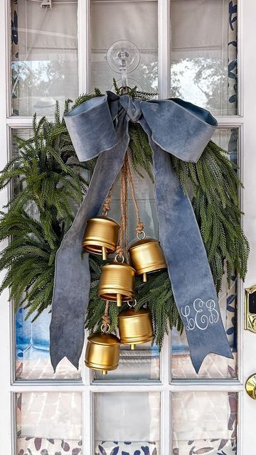 a christmas wreath with bells hanging from it's front door, in front of a window