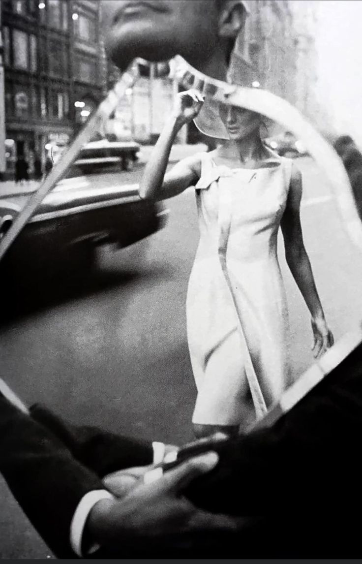 a black and white photo of a woman walking down the street with a man holding an umbrella over her head