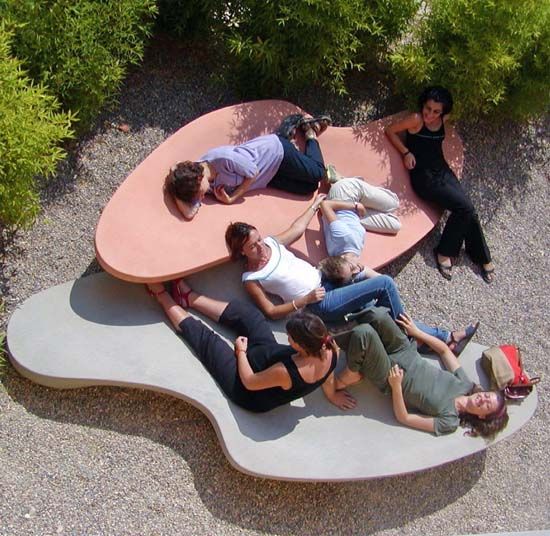 several people laying on top of a bench in a park