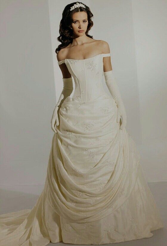 a woman in a white wedding dress with gloves on her head is standing and looking off to the side