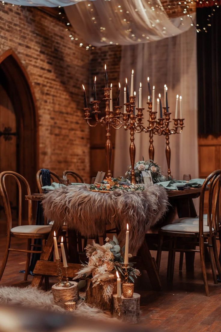 a dining room table with candles and fur on it, surrounded by other chairs in front of a brick wall