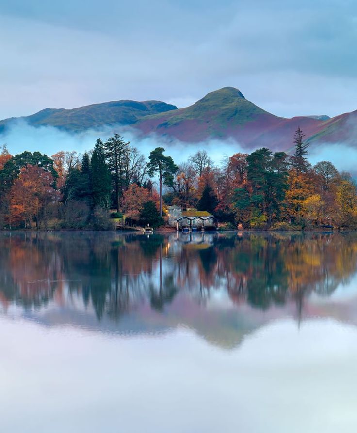 a lake surrounded by mountains with trees in the foreground and clouds in the background