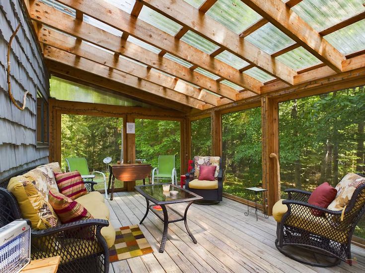 a covered porch with wicker furniture and lots of trees in the backgroud