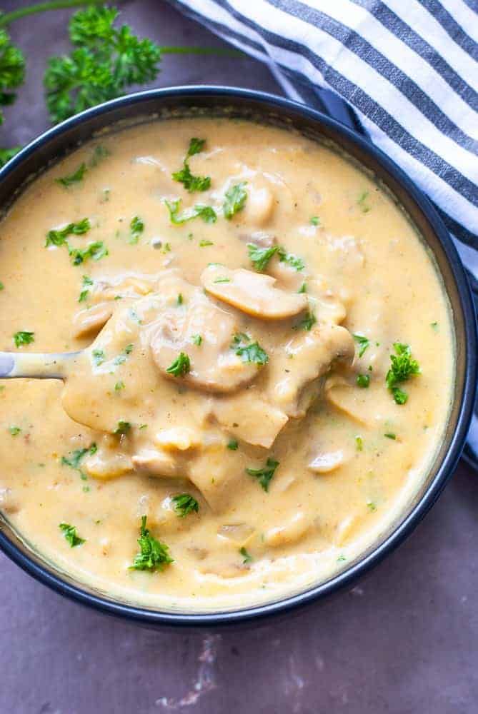 a blue bowl filled with creamy chicken and broccoli soup on top of a gray surface