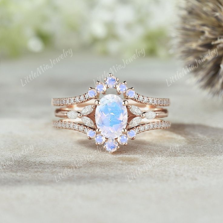 a white opal and diamond ring set on top of a table next to a pine cone